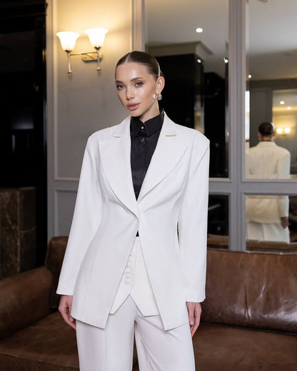 Woman in a white suit standing in a room with a mirror and lamp.