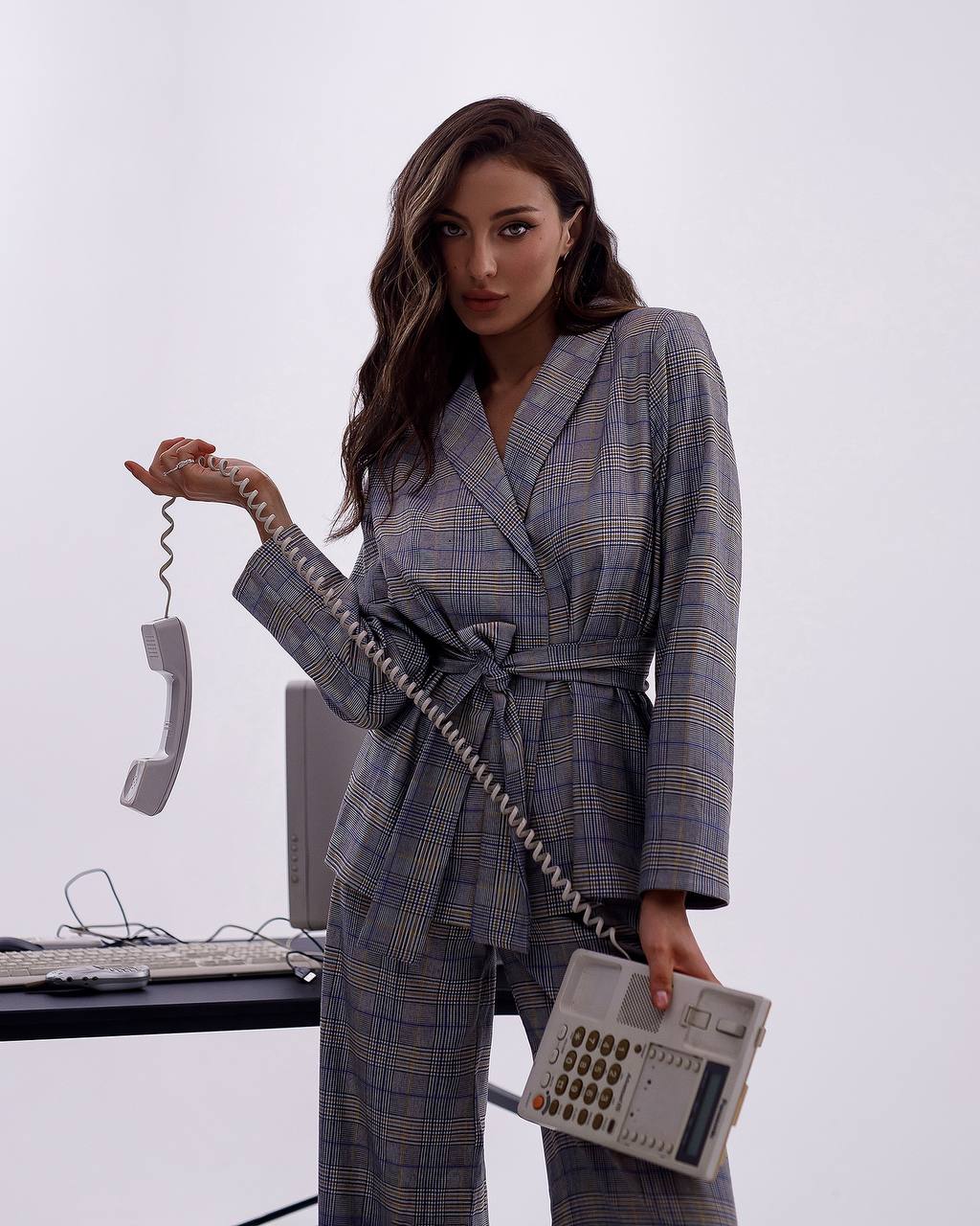 Woman in a plaid suit holding a vintage telephone with a white background