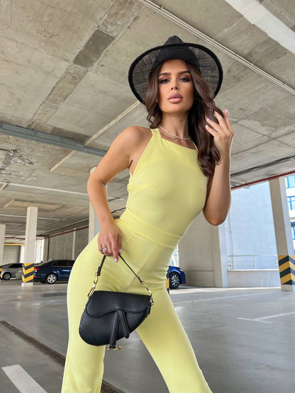 Woman in a yellow outfit and black hat holding a black handbag in an underground parking lot.