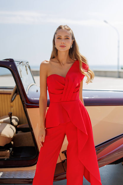 Woman in a red strapless jumpsuit standing in front of an open car door.