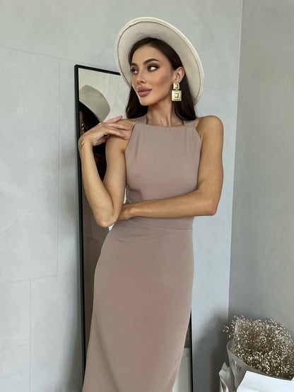 Woman in a beige dress and hat posing against a neutral wall.