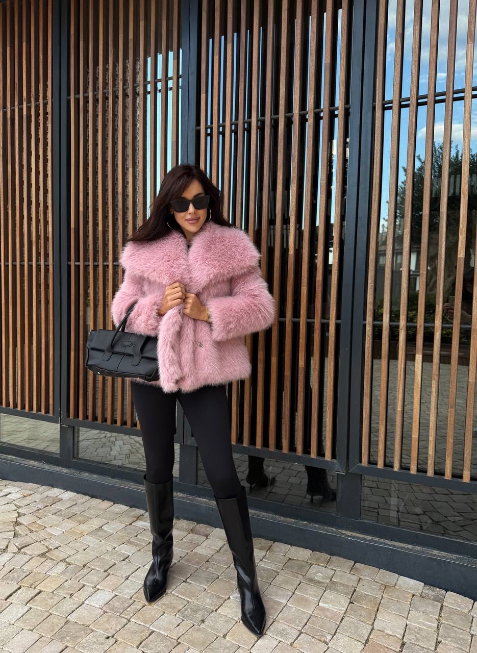 Woman wearing a pink fur coat and black outfit standing in front of a modern building.