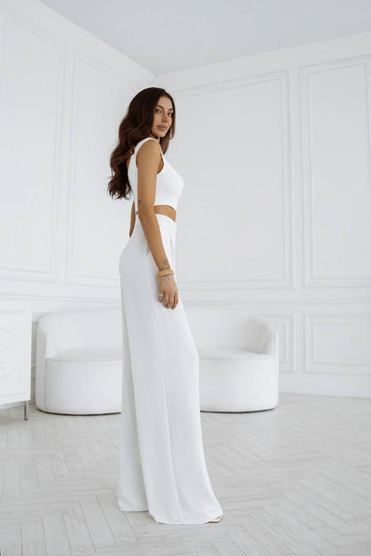 Woman in a white outfit standing in a minimalistic room with white walls and furniture.
