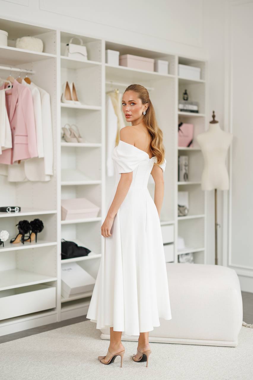Woman in a white off-shoulder dress standing in a stylishly organized closet.
