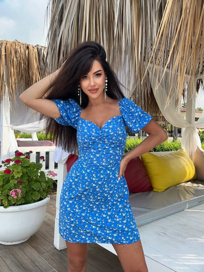 Woman in a blue dress standing outdoors with plants and furniture in the background