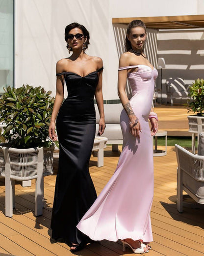 Two women in elegant evening gowns standing on a wooden deck with plants and chairs in the background.