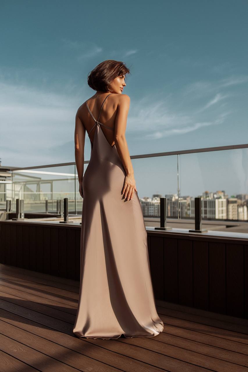 Woman in a beige evening gown standing on a rooftop with a cityscape in the background