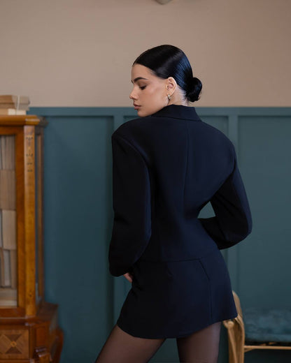 Woman wearing a navy blue blazer and skirt set in an indoor setting.