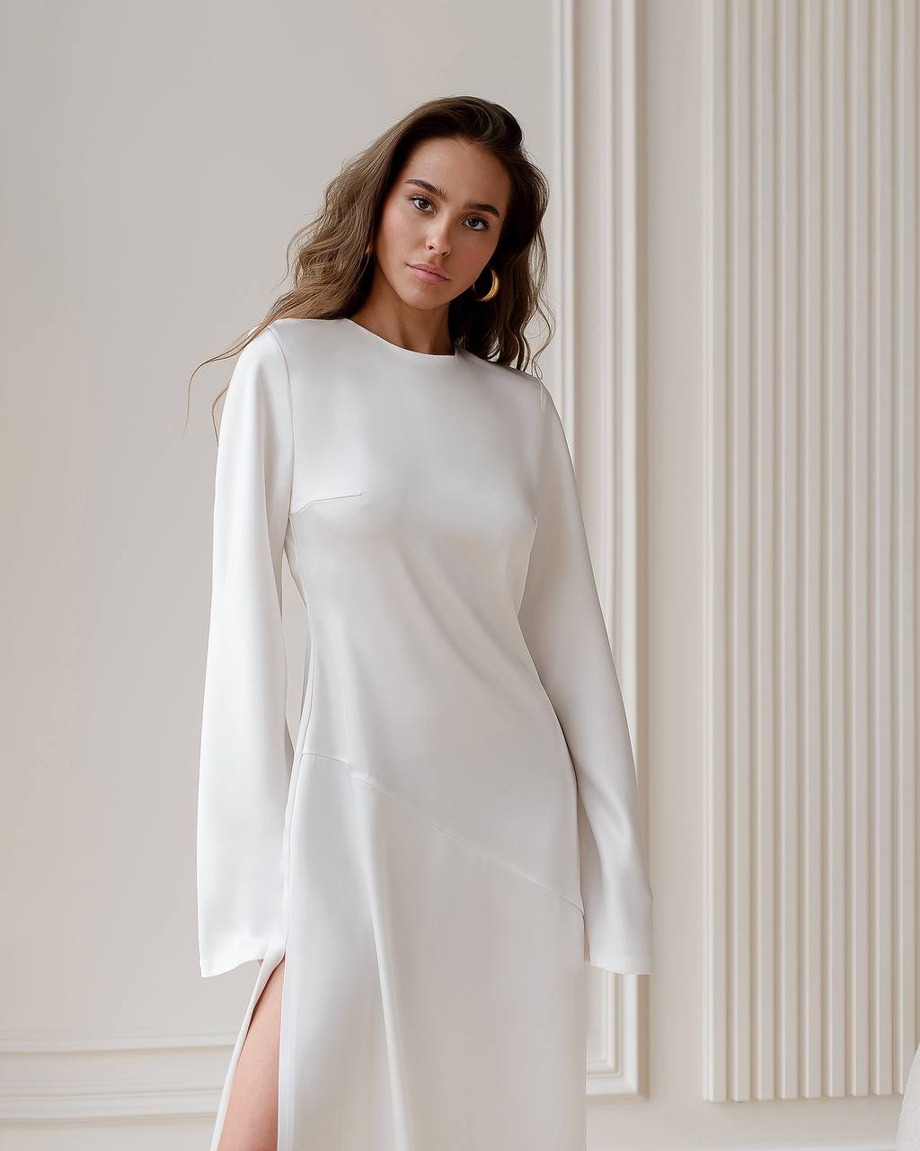 Woman wearing a white dress with long sleeves against a neutral background