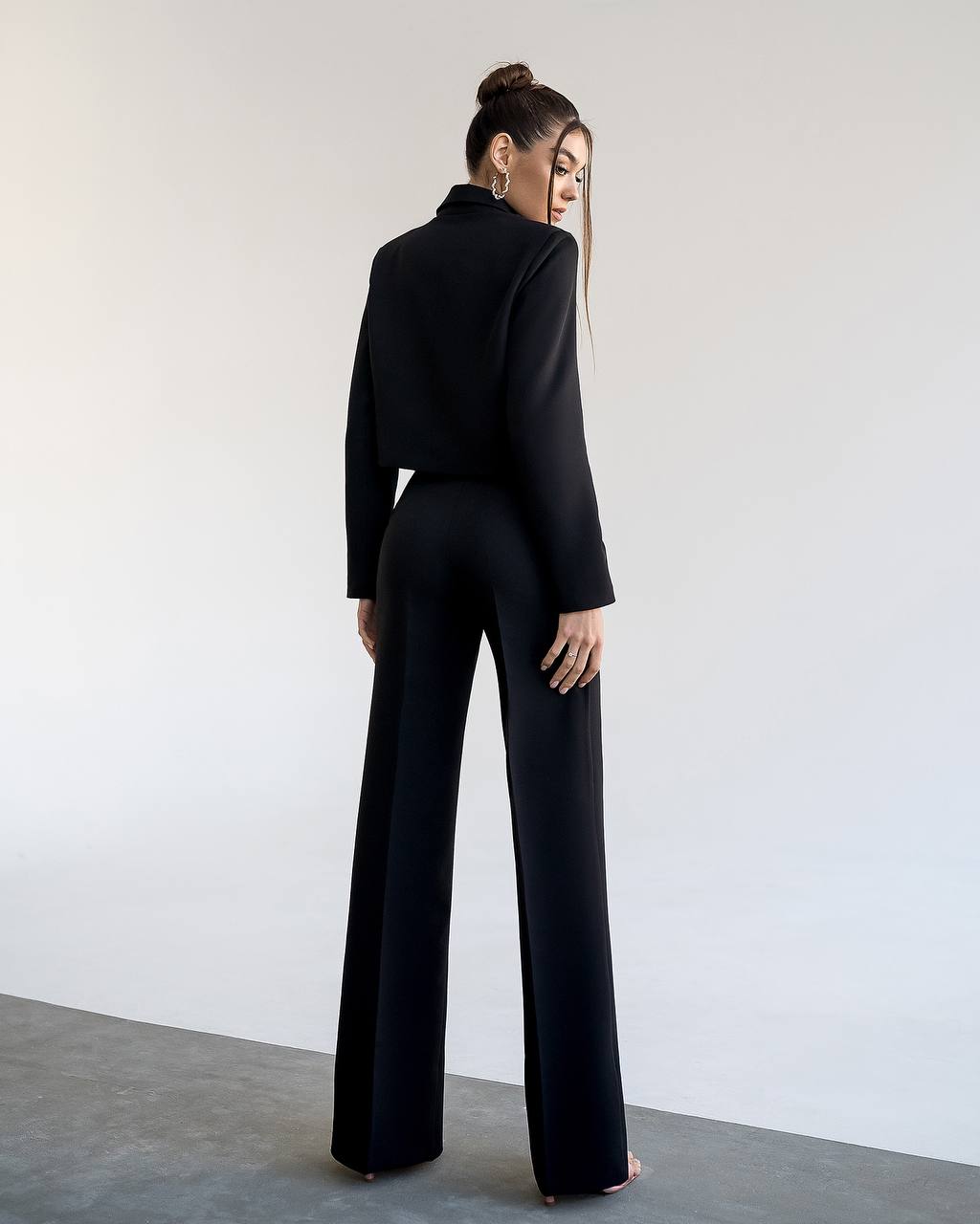Person wearing a black outfit with wide-leg pants against a plain background