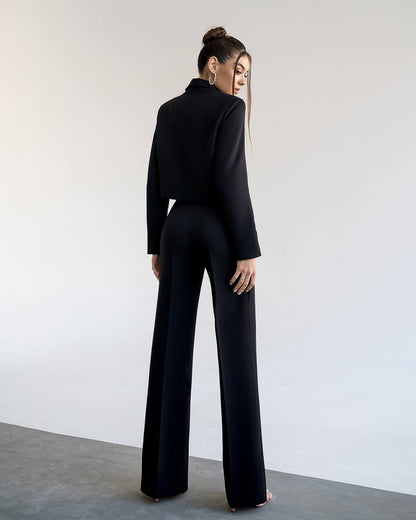 Person wearing a black outfit with wide-leg pants against a plain background