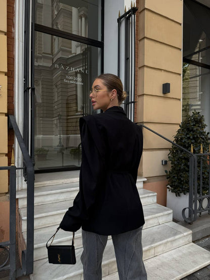 Woman in black coat and gray pants standing on steps outside a building with 'Baztan' sign.