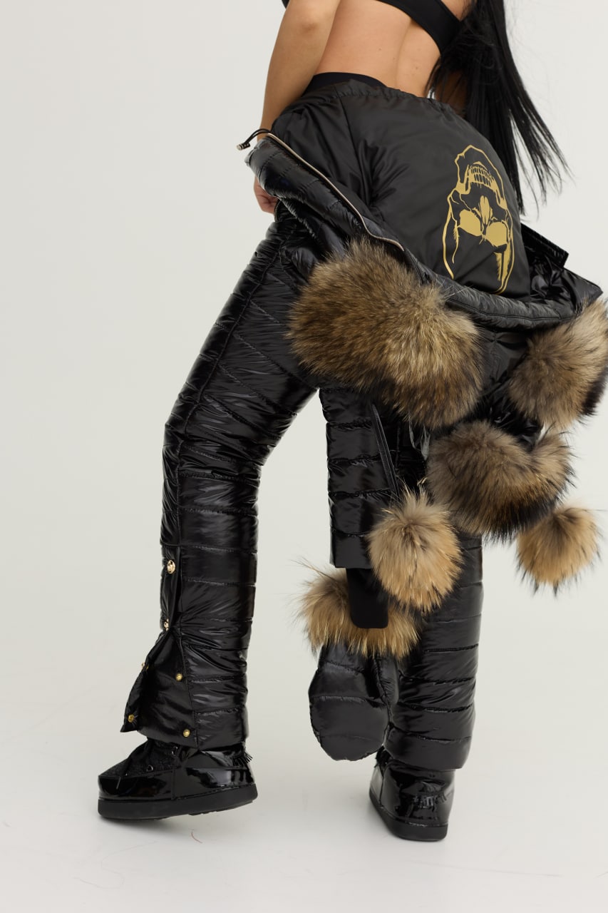 Black snow pants with fur accents worn by a person on a white background