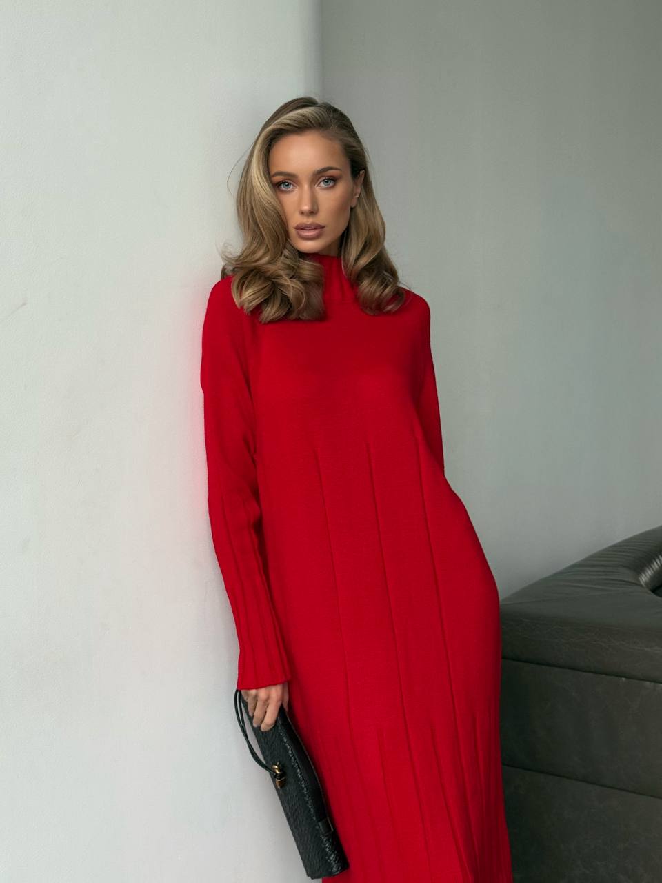 Woman in a red dress holding a black clutch against a neutral background