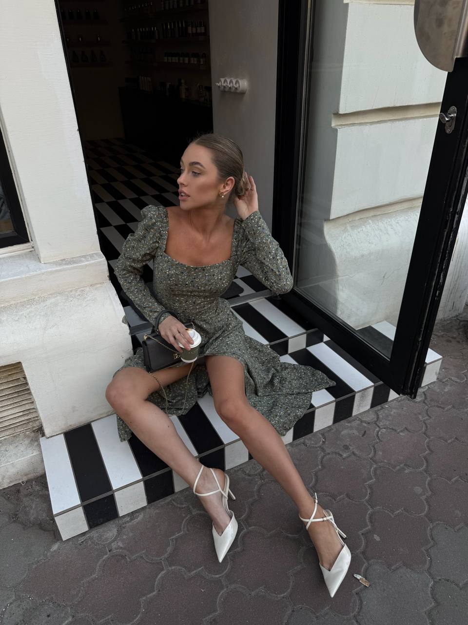 Woman sitting on black and white striped steps wearing a green dress and white shoes.