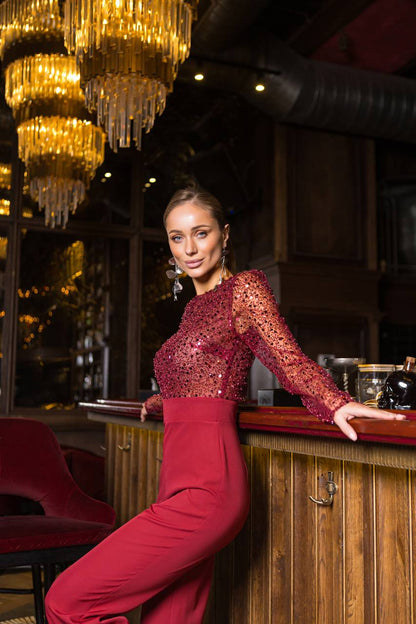 Woman in a red dress standing behind a bar with chandeliers above.