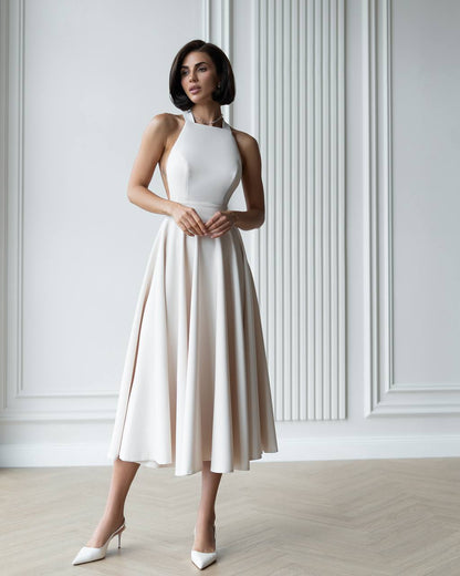 Woman wearing a white dress with a beige skirt against a light-colored wall.