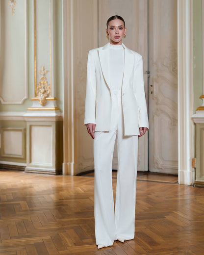 Person wearing a white suit standing in an elegant room with wooden flooring and decorative walls.