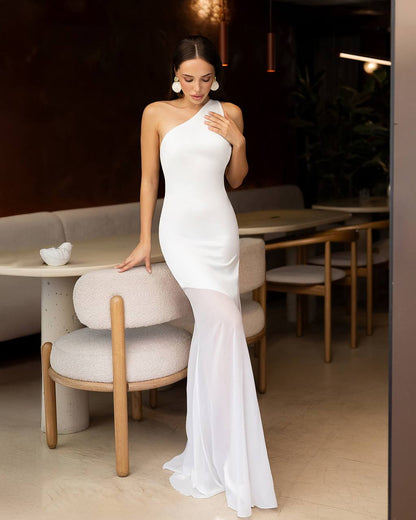 Woman in a white one-shoulder dress standing in a modern restaurant setting.