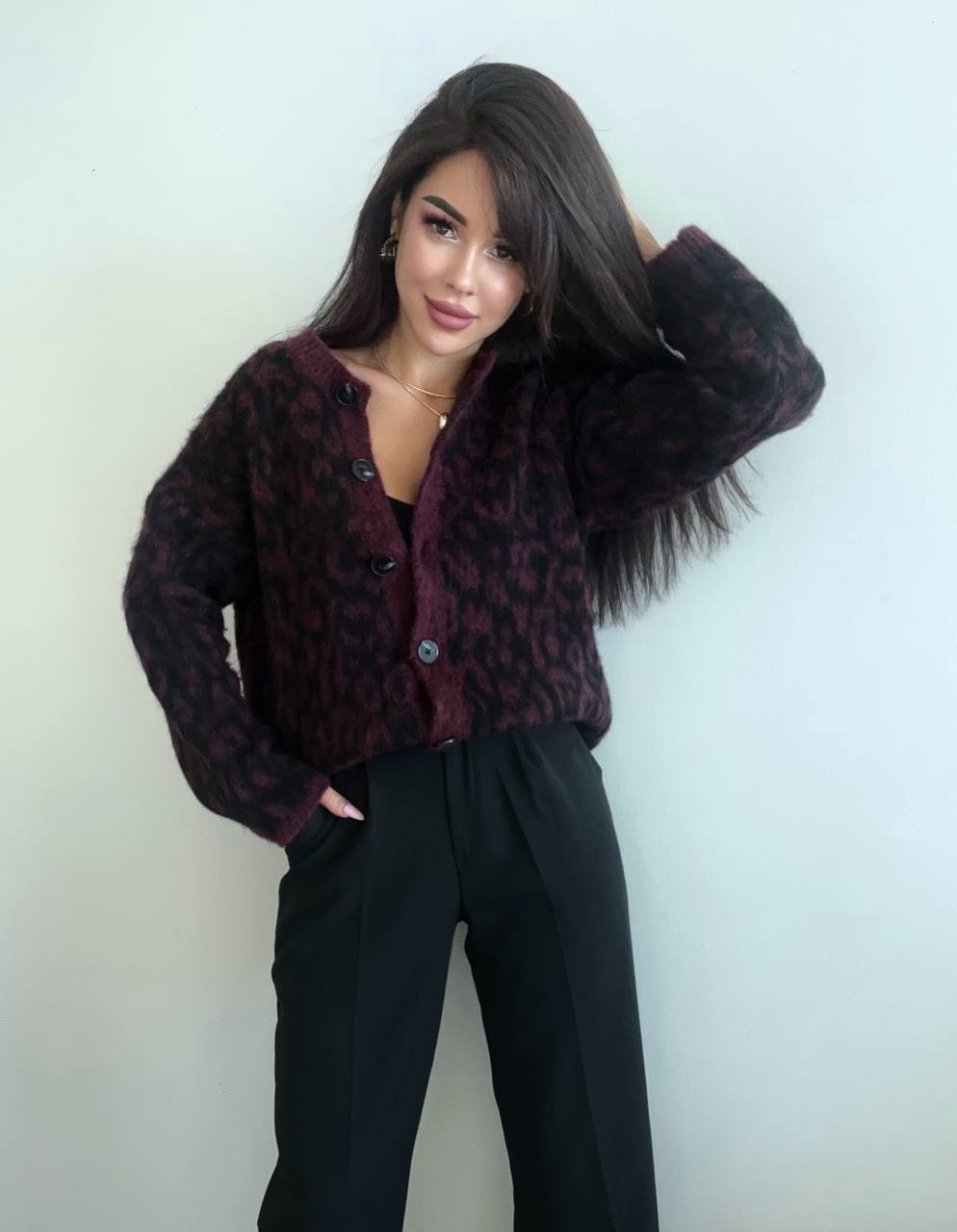 Woman wearing a patterned jacket and black pants against a plain background