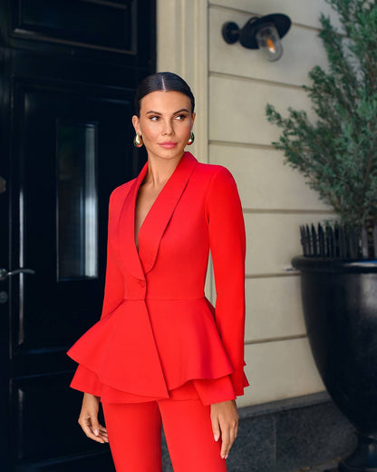 Woman in a red suit standing outside a building with a plant in the background
