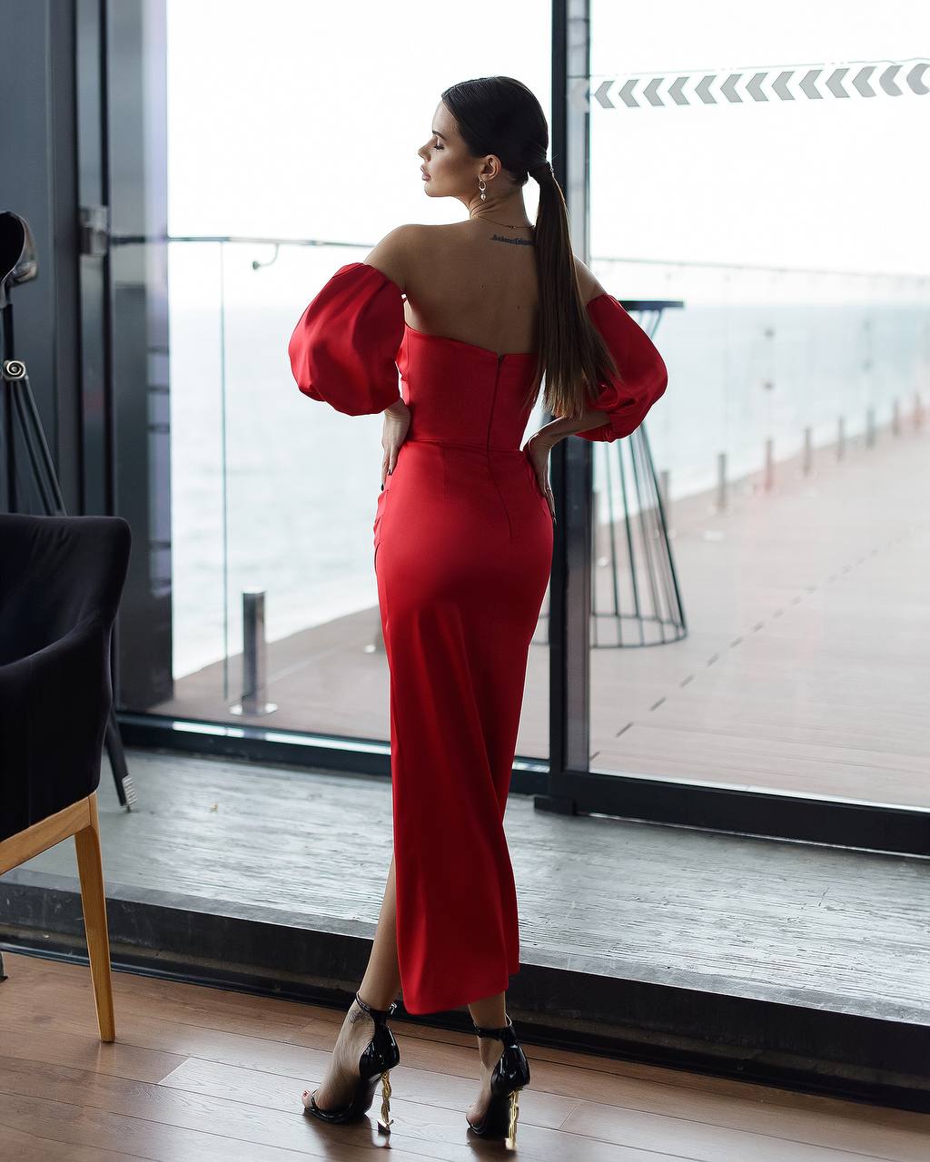 Woman in a red dress standing by a large window with a view of a dock.