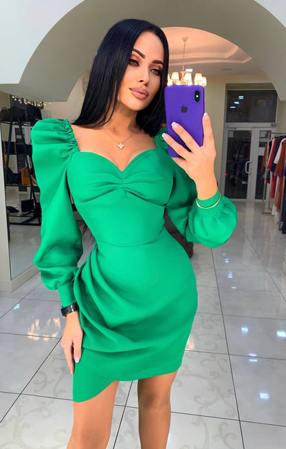 Woman taking a mirror selfie wearing a green dress in a shopping mall.