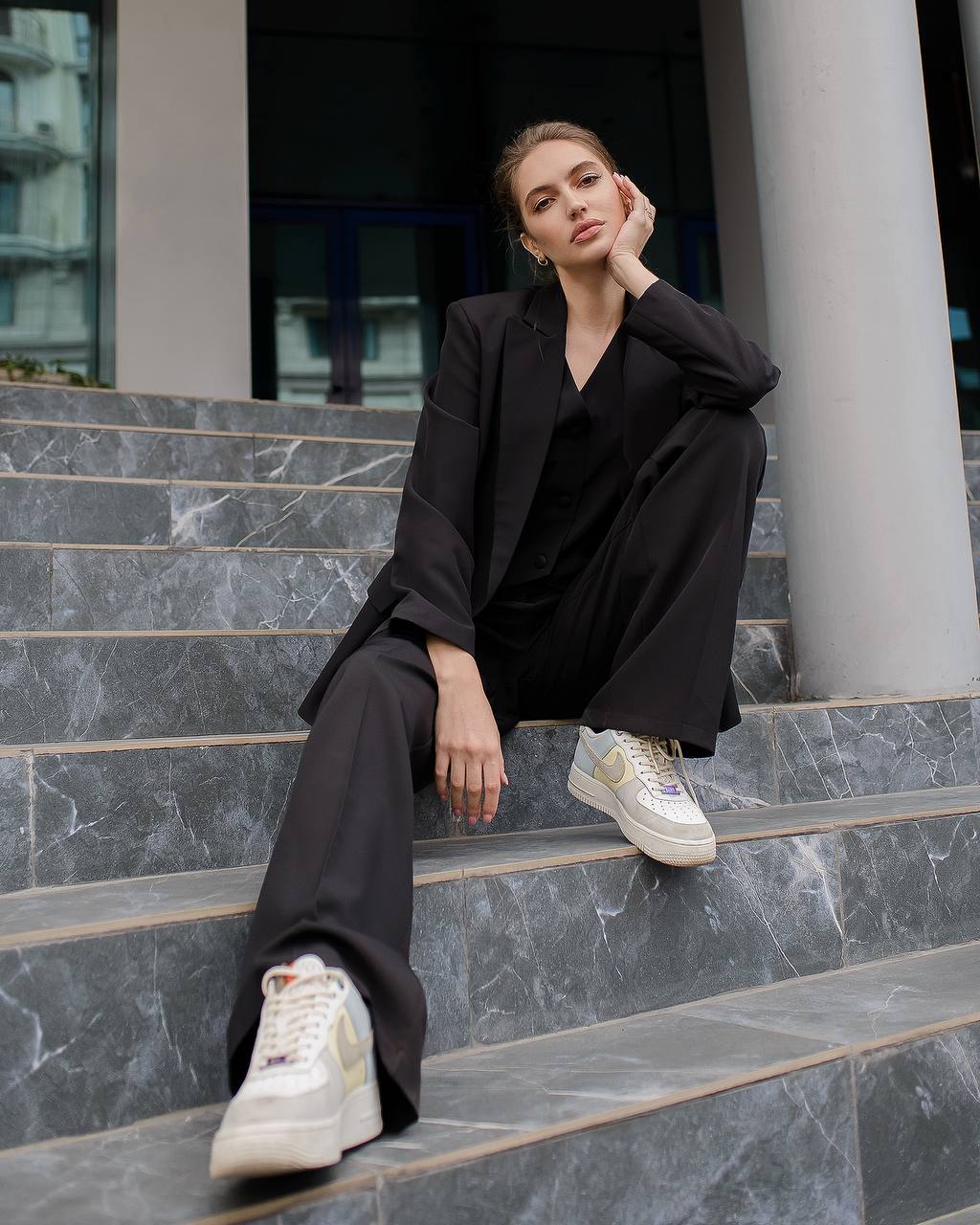 Woman in black outfit with white sneakers sitting on marble steps.