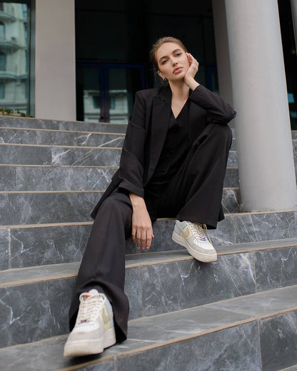 Woman in black outfit with white sneakers sitting on marble steps.