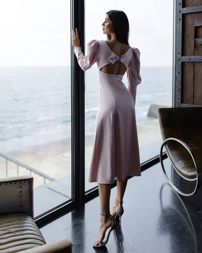 Woman in a pink dress standing by a large window with a view of the ocean.