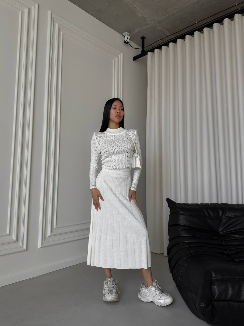 Woman in a white outfit standing in a room with a black bean bag chair.