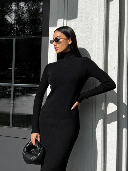 Woman in a black dress standing against a gray wall
