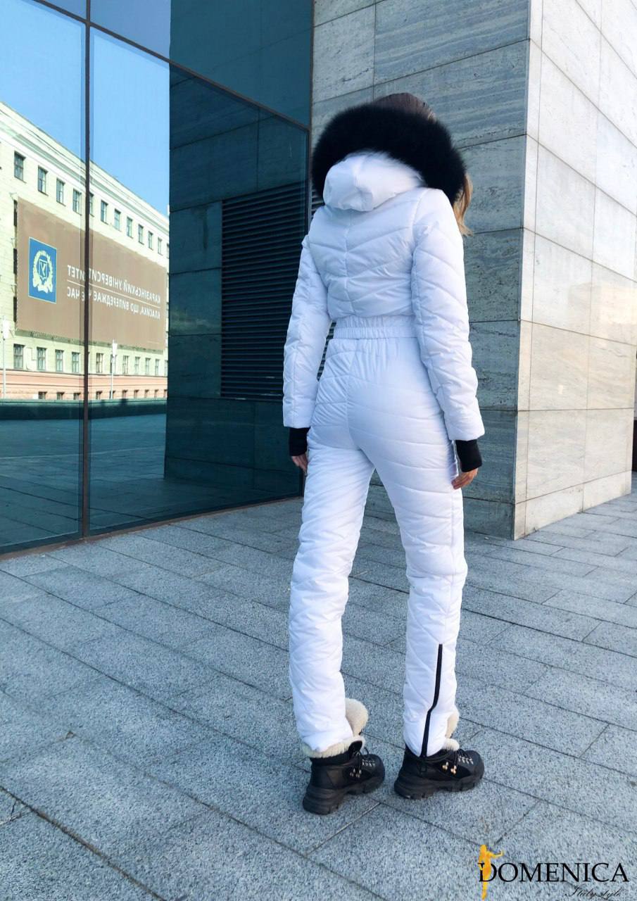 Person wearing a white puffer suit standing in front of a modern building.