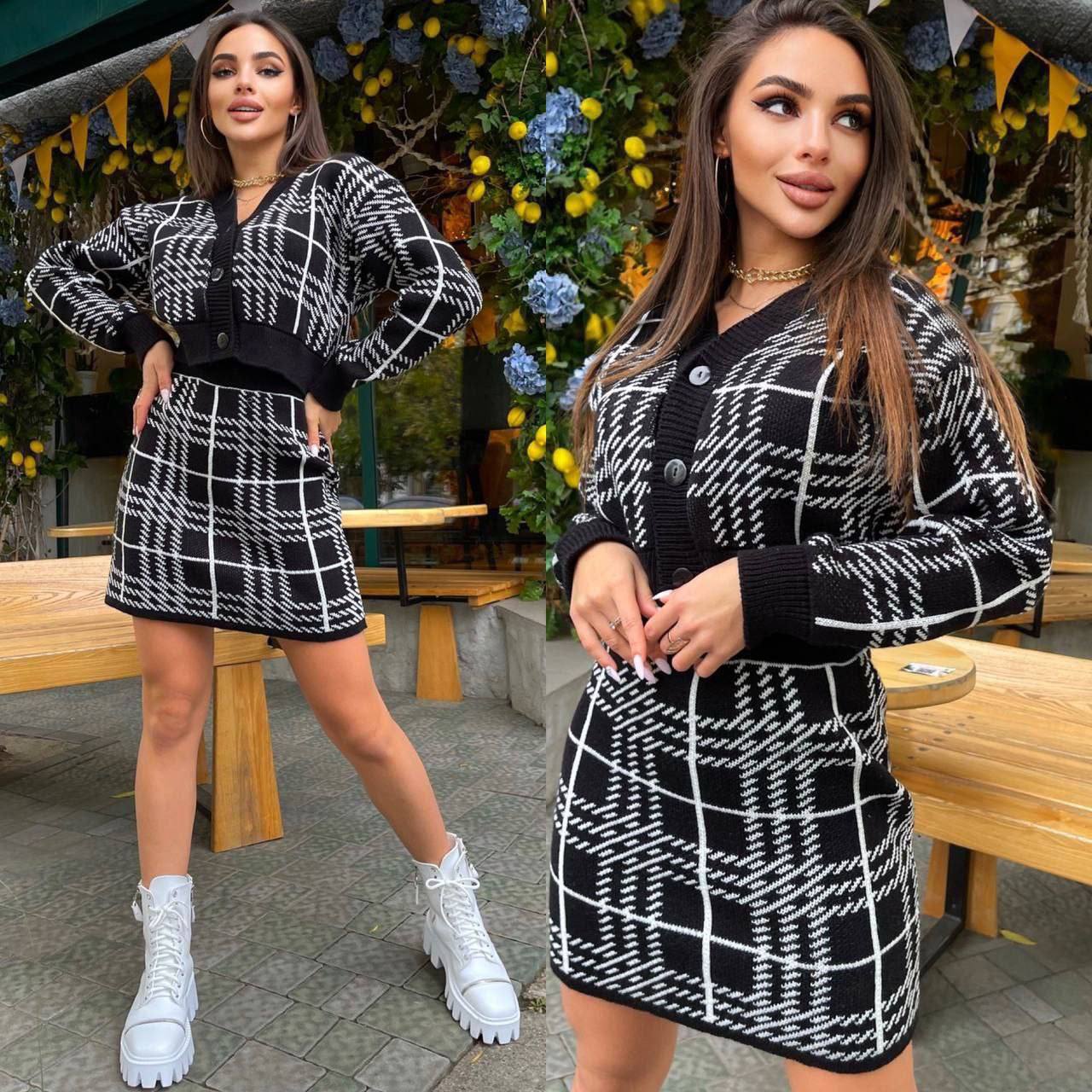 Woman wearing a black and white checkered dress with a matching cardigan in an outdoor setting.