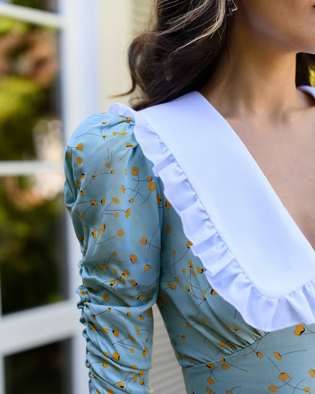 Close-up of a person wearing a light blue dress with ruffled white collar and long sleeves.
