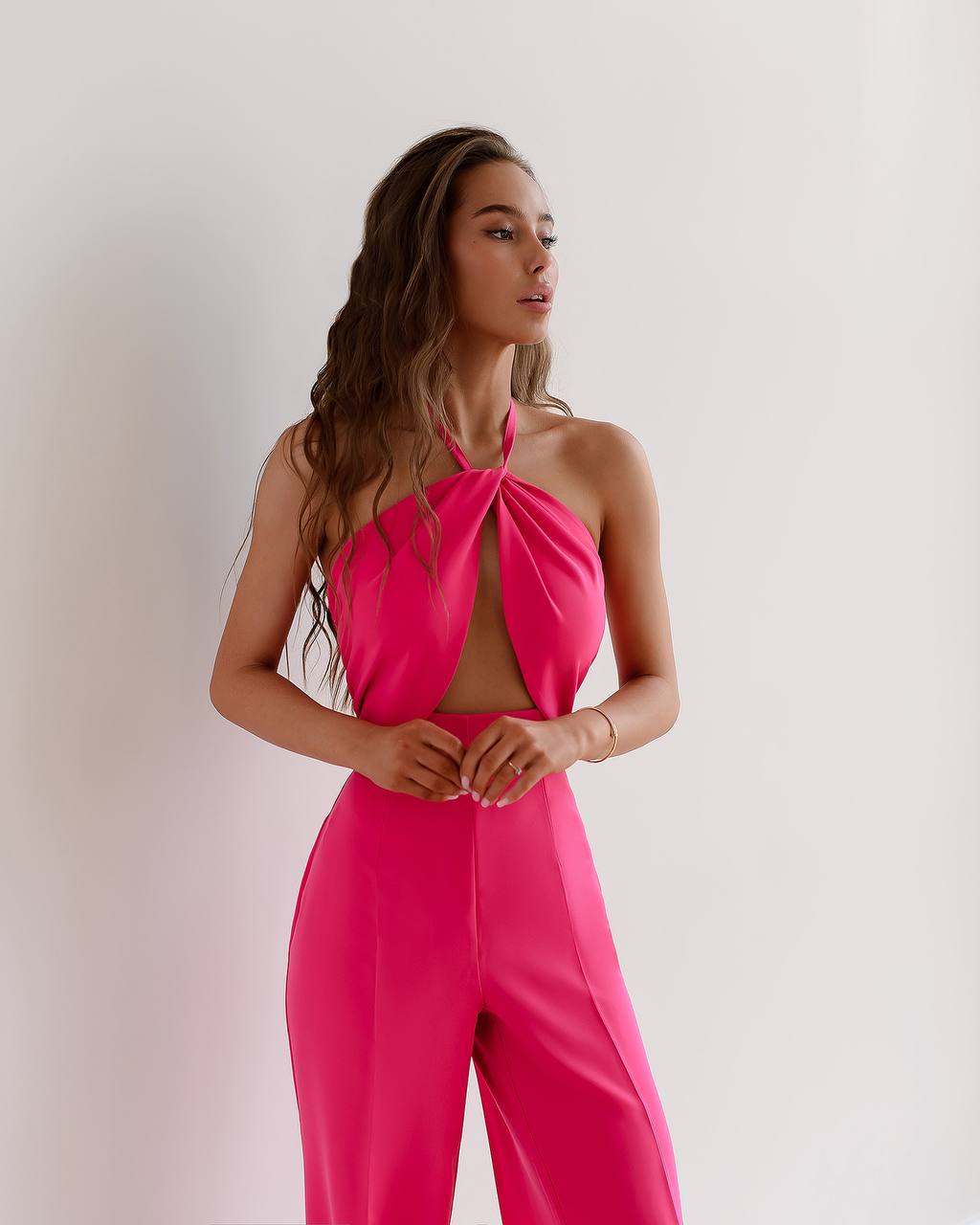 Woman wearing a bright pink jumpsuit against a plain background