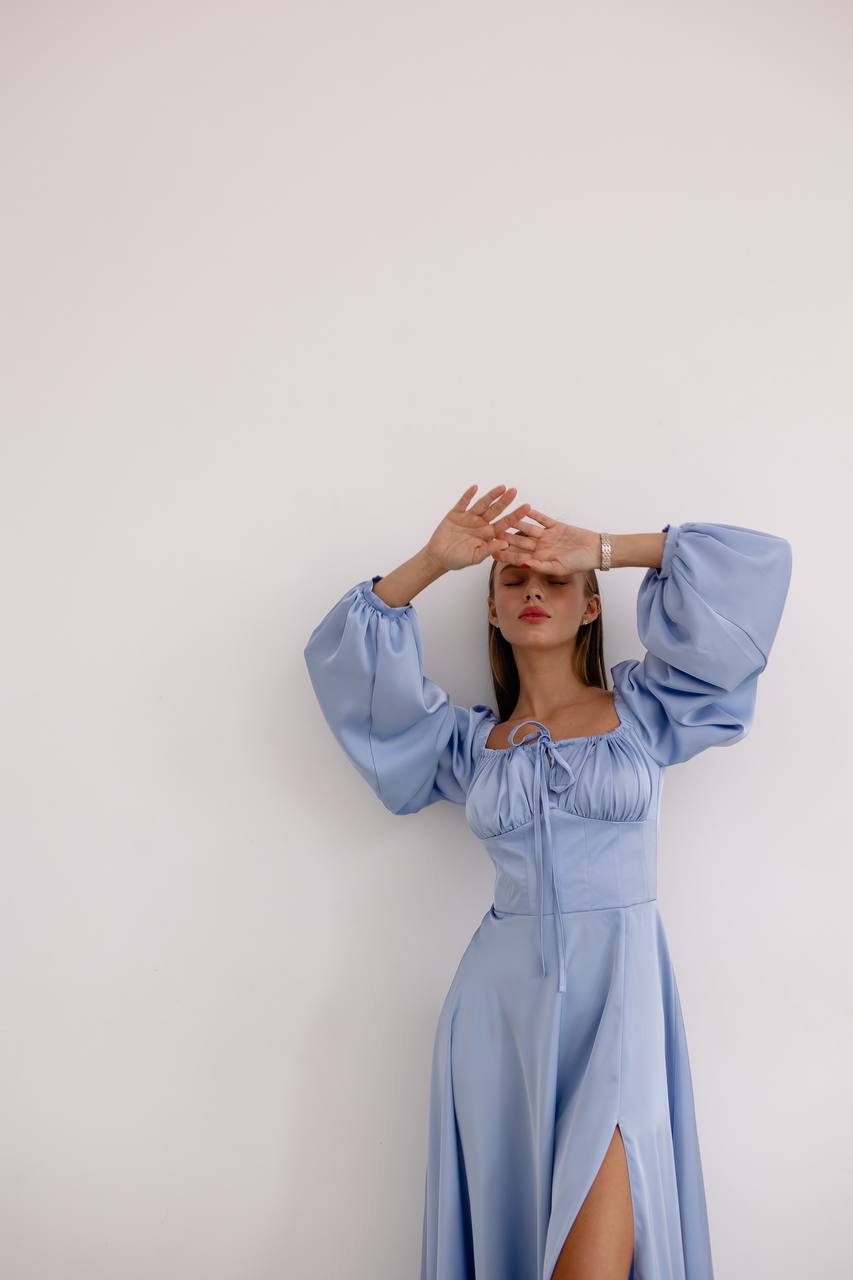 Woman wearing a light blue dress with wide sleeves against a white background