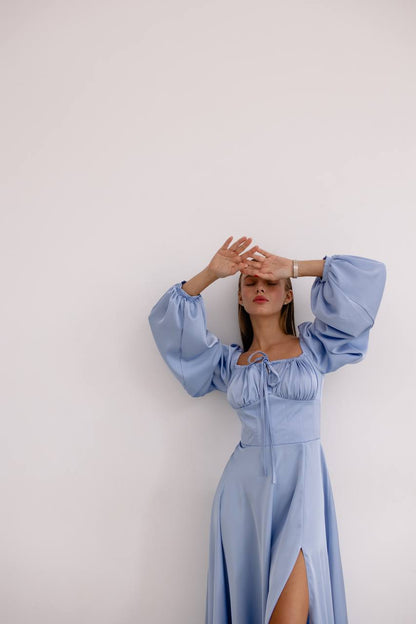 Woman wearing a light blue dress with wide sleeves against a white background