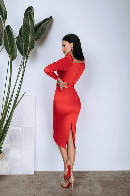 Woman in a red dress standing next to a plant against a white wall