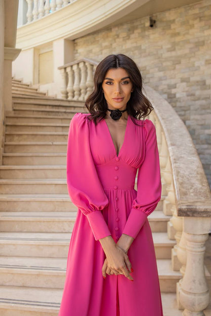Woman in a pink dress standing on a staircase with stone walls.