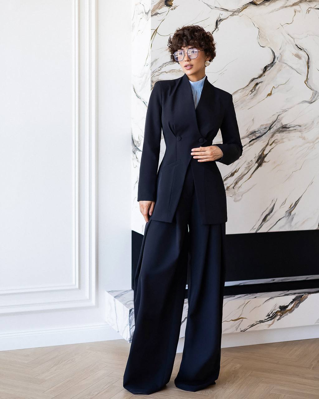 Person wearing a navy blue suit standing against a marble wall.