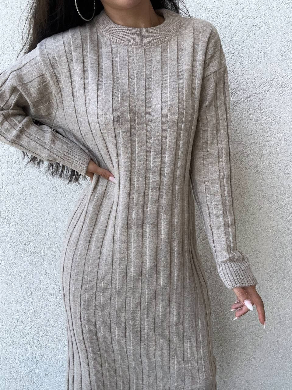 Person wearing a beige ribbed sweater dress against a white wall