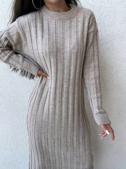 Person wearing a beige ribbed sweater dress against a white wall