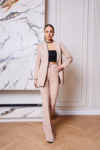 Woman in a beige suit standing in a stylish interior setting with marble wall.