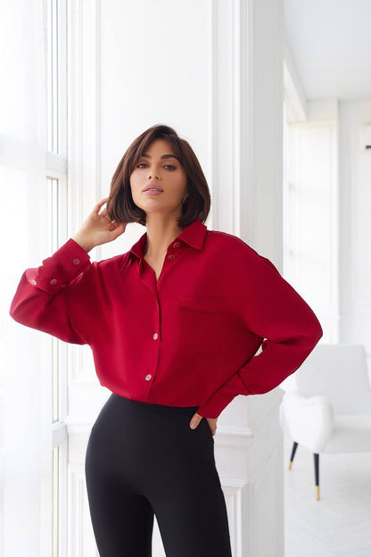 Woman wearing a red blouse and black pants in a bright room.