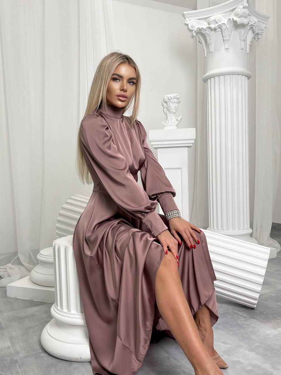 Woman in a mauve dress sitting on white steps in a classical setting