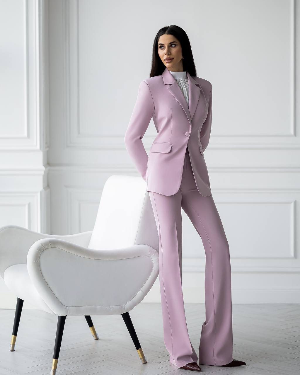 Woman in a pink suit standing in a room with white walls and a white chair.