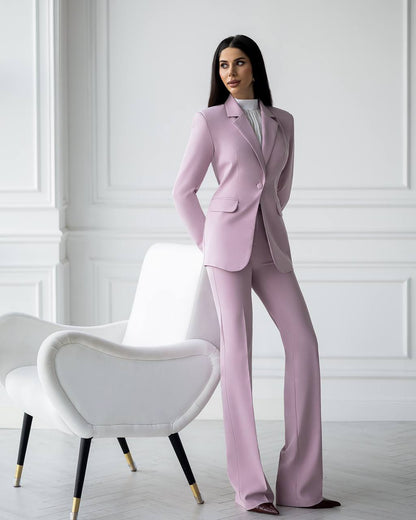 Woman in a pink suit standing in a room with white walls and a white chair.