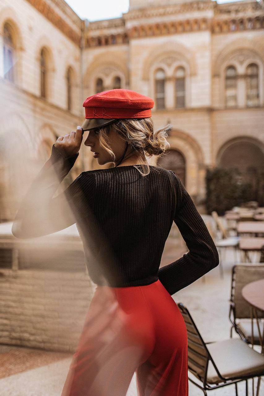 Person wearing a red cap and red pants standing in an outdoor setting with a building in the background.