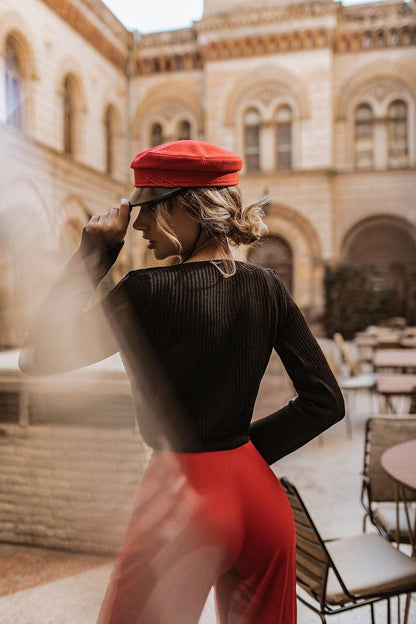 Person wearing a red cap and red pants standing in an outdoor setting with a building in the background.